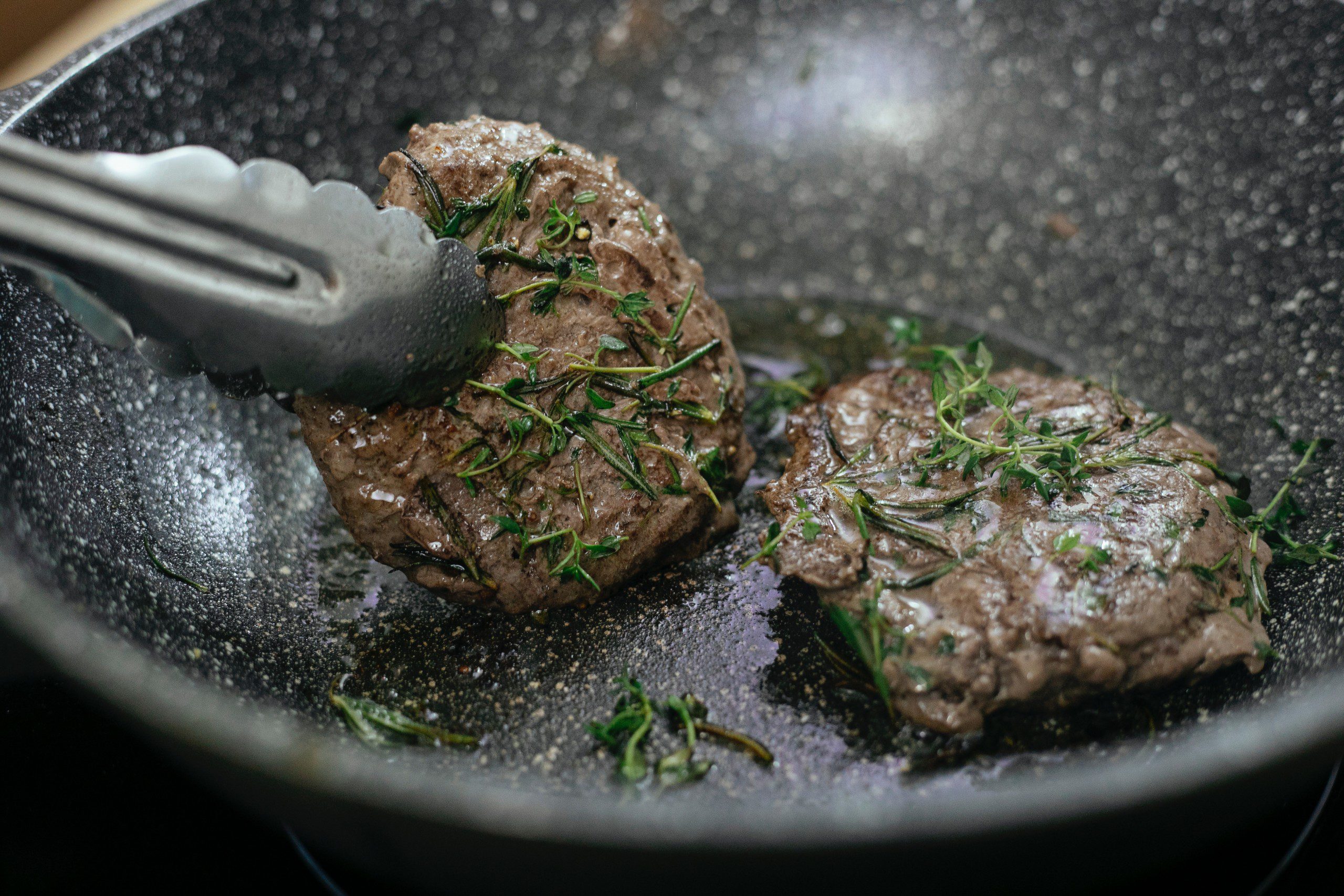 Imagem de uma panela com dois pedaços de carne temperados com alecrim. 