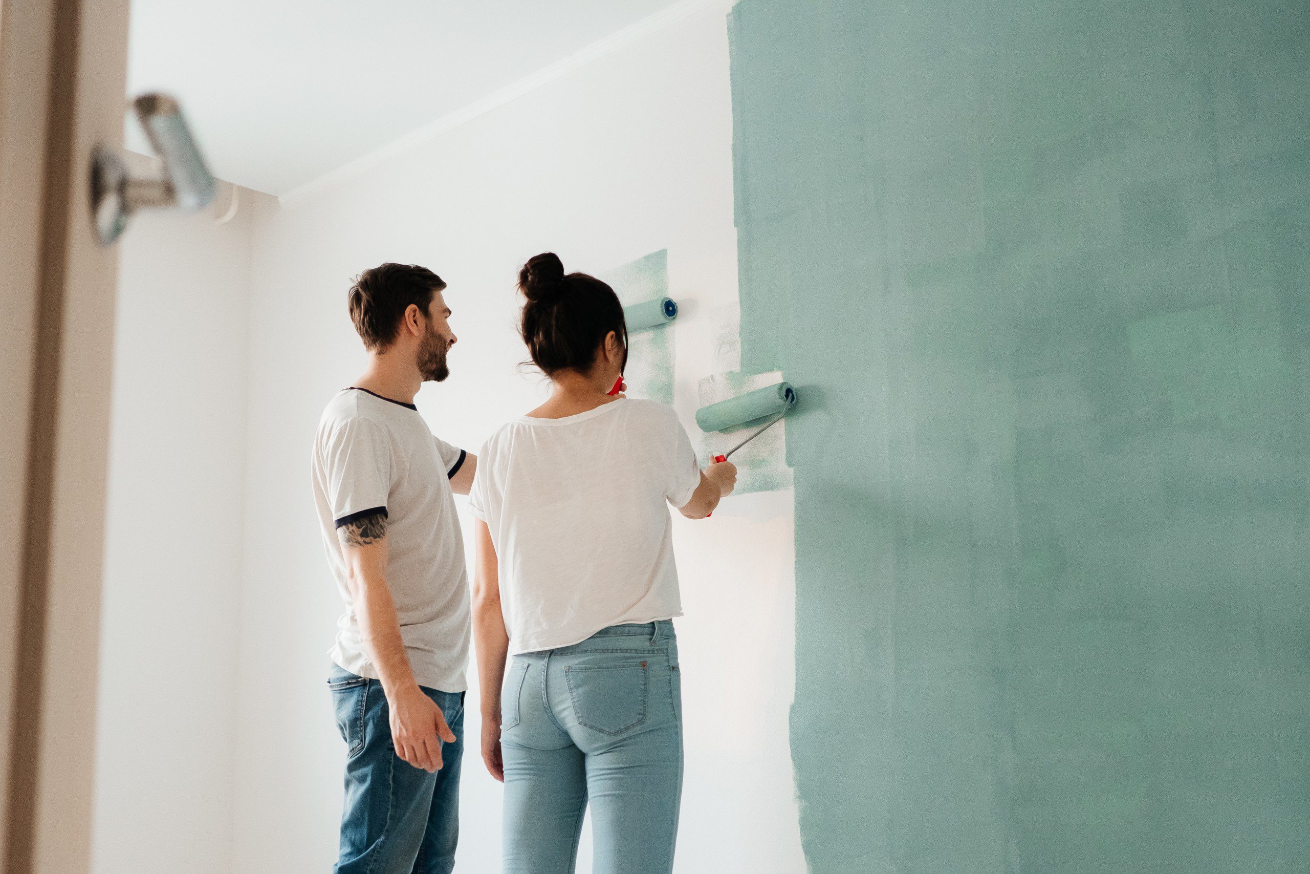 Imagem de um casal pintando a parede da casa com tinta de cor verde.