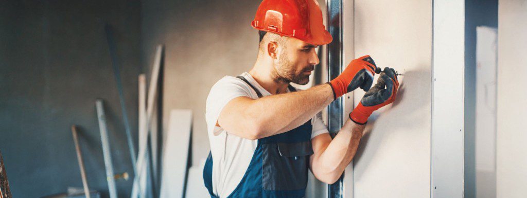 Imagem de um homem fixando os perfis para instalar painéis de drywall. 