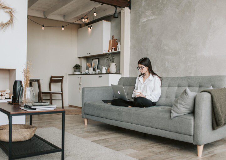 Foto de uma sala de estar moderna em tons de cinza e elementos em madeira. Na foto há uma mulher sentada no sofá cinza, há também um tapete e uma mesa de centro.