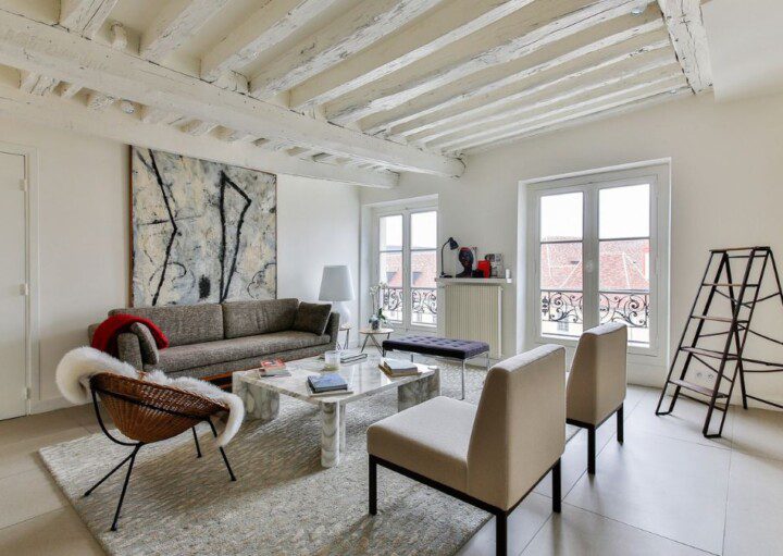 ambiente com sofás, cadeiras e decoração escandinava, paredes claras, móveis de madeira e janelas amplas