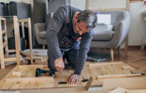 Imagem de um senhor montando uma mesa de madeira.