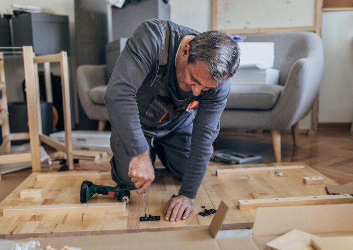 Imagem de um senhor montando uma mesa de madeira.