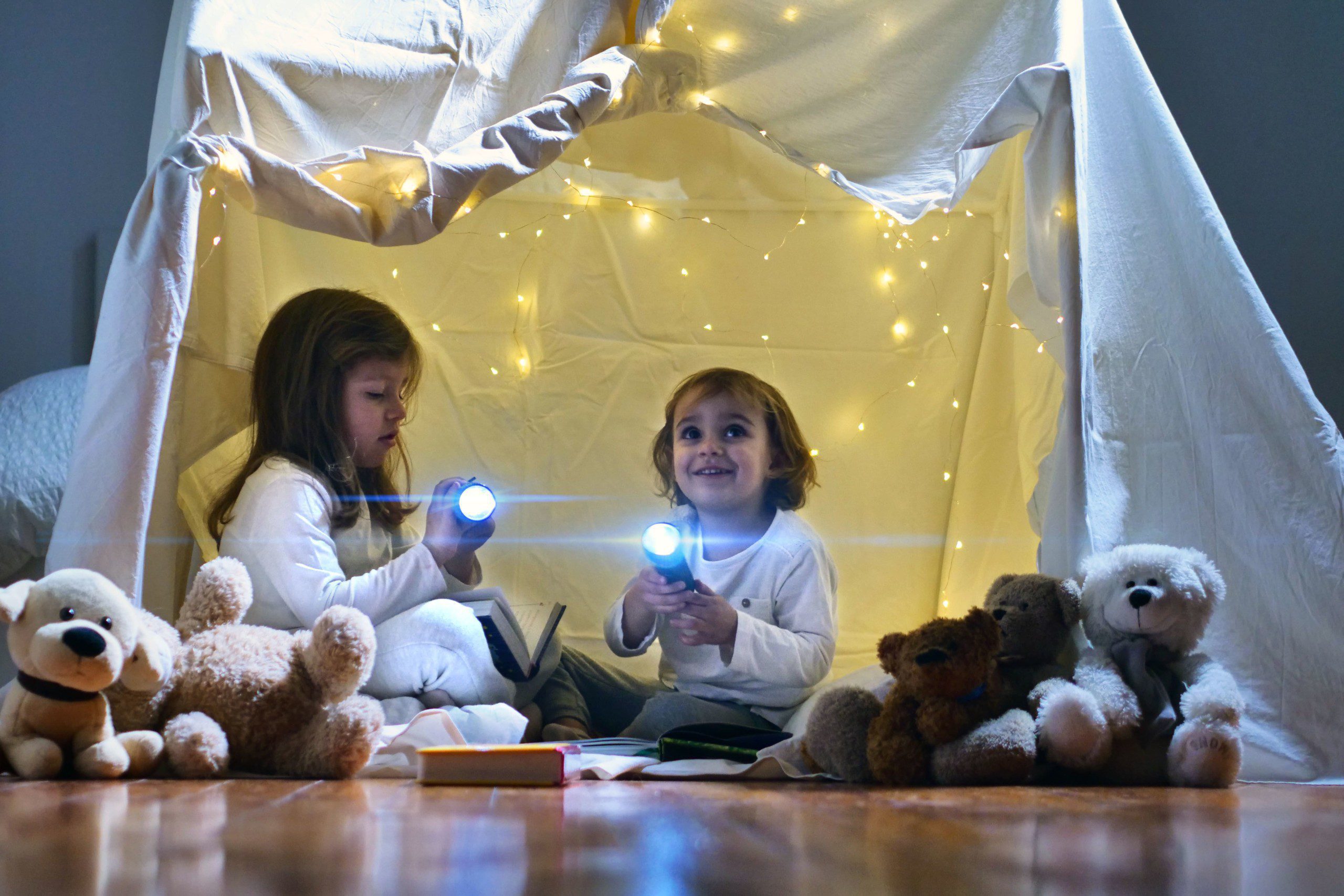 Imagem de duas meninas brincando em uma cabaninha feita com lençol.