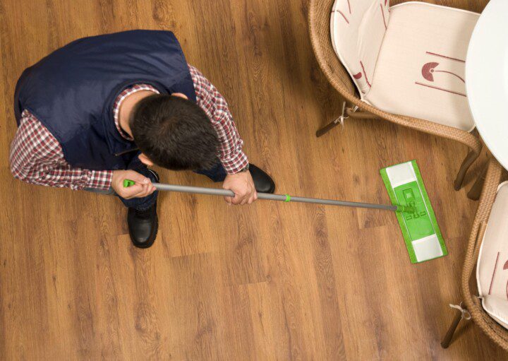 Imagem de um homem limpando um piso laminado com estilo amadeirado.