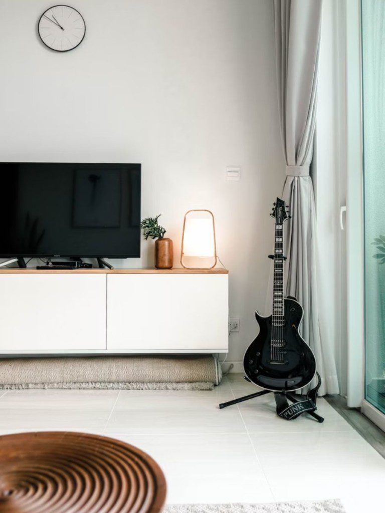 Sala escandinava com tapete branco, guitarra, televisão e tapete de madeira, com cortinas laterais