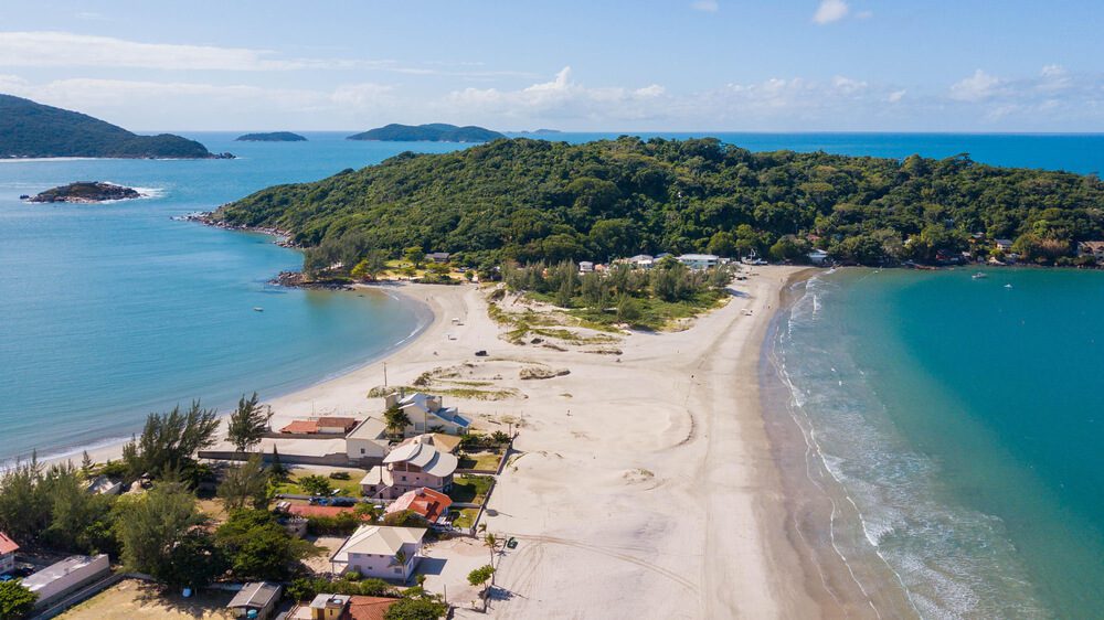 Foto que ilustra matéria sobre as praias de Palhoça mostra a Península que liga o continente à Ilha dos Papagaios Grande (ao fundo). À esquerda você vê a Praia do Sonho. E à direita a Praia da Ponta do Papagaio.