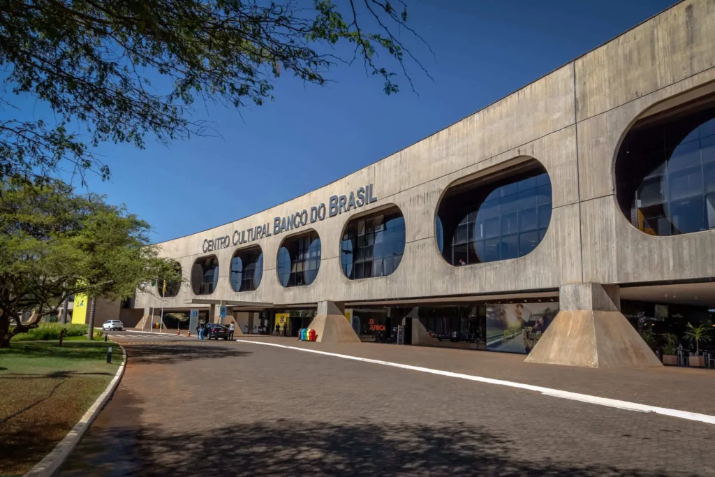 Imagem do prédio do Centro Cultural Branco do Brasil - Brasília, o CCBB Brasília, sob um céu azul claro, com árvores por perto e pessoas na entrada