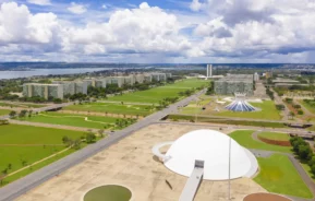 Imagem da vista aérea de Brasília, Brasil, destacando os prédios governamentais modernistas, a cúpula branca do Museu Nacional, a Catedral de Brasília e os gramados verdes para ilustrar matéria sobre os melhores bairros de Brasília