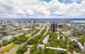 Imagem da vista aérea de Brasília com avenidas largas, prédios altos e árvores verdejantes sob nuvens esparsas para ilustrar matéria sobre o que fazer em Brasília