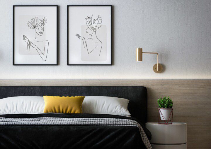 quarto com decoração minimalista. Cama com coberta preta e almofadas amarelas, quadros acima da cama com desenhos e pequena mesa com planta