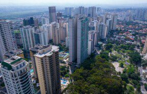 Foto que ilustra matéria sobre bairros de São José dos Campos mostra uma vista aérea da Praça Ulisses Guimarães, no bairro Jardim Aquarius, uma área arborizada que aparece no canto direito da imagem e tem ao lado, na esquerda, altos prédios residenciais.