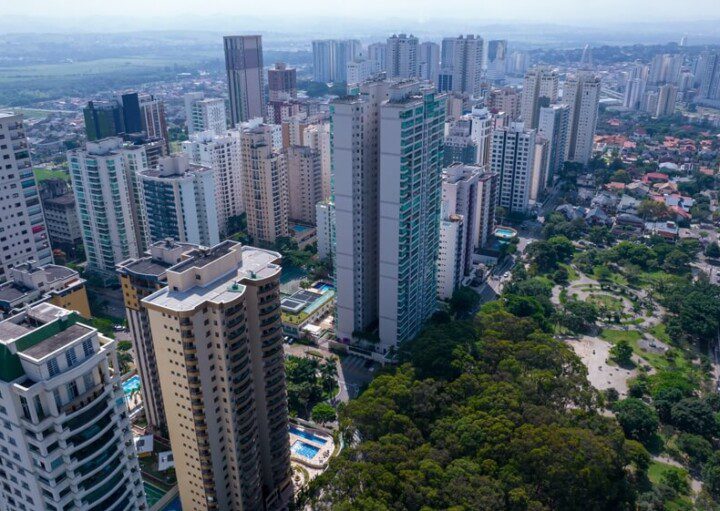 Foto que ilustra matéria sobre bairros de São José dos Campos mostra uma vista aérea da Praça Ulisses Guimarães, no bairro Jardim Aquarius, uma área arborizada que aparece no canto direito da imagem e tem ao lado, na esquerda, altos prédios residenciais.