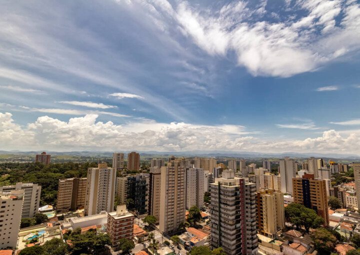 Foto que ilustra matéria sobre custo de vida em São José dos Campos mostra uma visão do alto da cidade, onde aparecem grandes prédios. Ao fundo, um céu azul com algumas poucas nuvens brancas.