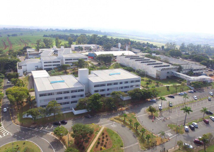 Foto que ilustra matéria sobre Faculdades em Campinas mostra uma visão aérea do Campus I da PUC-Campinas, um conjunto de prédios cercados por áreas de estacionamentos e áreas gramadas.