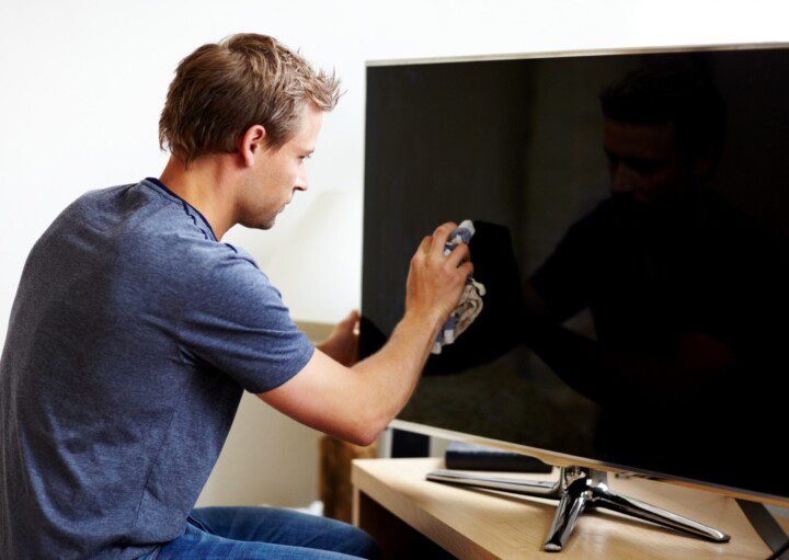 Imagem de um homem limpando a tela de uma TV com uma flanela.