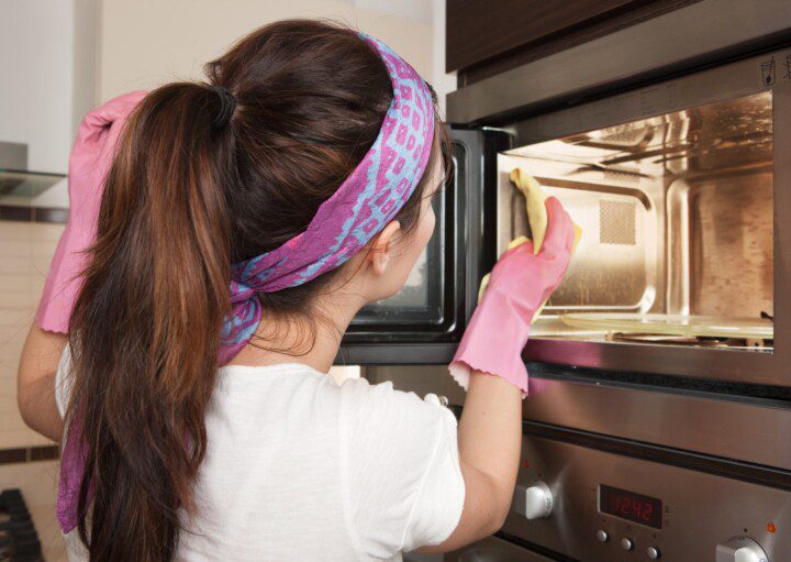 Imagem de uma mulher limpando microondas por dentro com luvas de proteção.