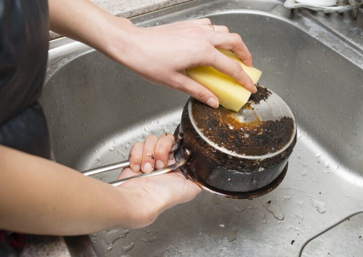 Imagem de uma mulher limpando uma panela queimada com esponja.