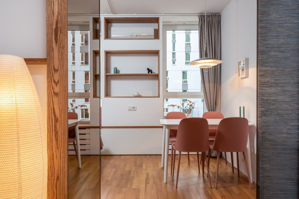 A foto mostra um exemplo de decoração retrô em uma kitnet com uma mesa com 4 cadeiras, estante e luminária de chão.