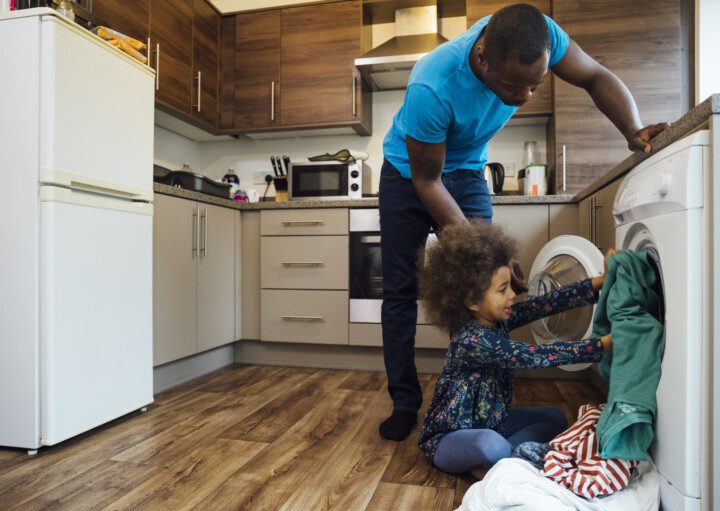 foto que ilustra matéria sobre cozinha com lavanderia mostra um homem e um menino colocando roupa para lavar