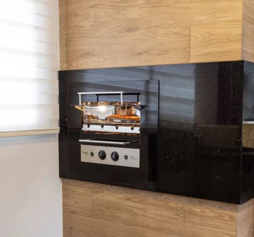 Foto que ilustra matéria sobre tipos de granito mostra uma churrasqueira a gás revestida por um granito preto e embutida em uma parede.