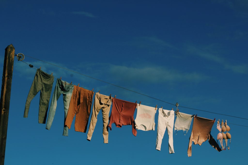 Varal com roupas como calças e blusas e, ao fundo, céu azul. Foto disponível no Unsplash