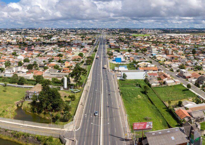 Foto que ilustra matéria sobre os bairros de Pinhais mostra uma panorâmica da cidade, com destaque para a Rodovia Deputado João Leopoldo, a principal via da região.