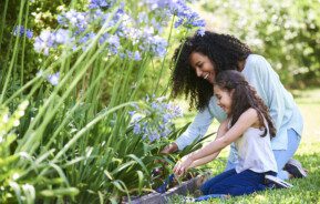 Foto que ilustra matéria sobre jardim no quintal mostra uma mulher e uma criança plantando em um jardim no quintal