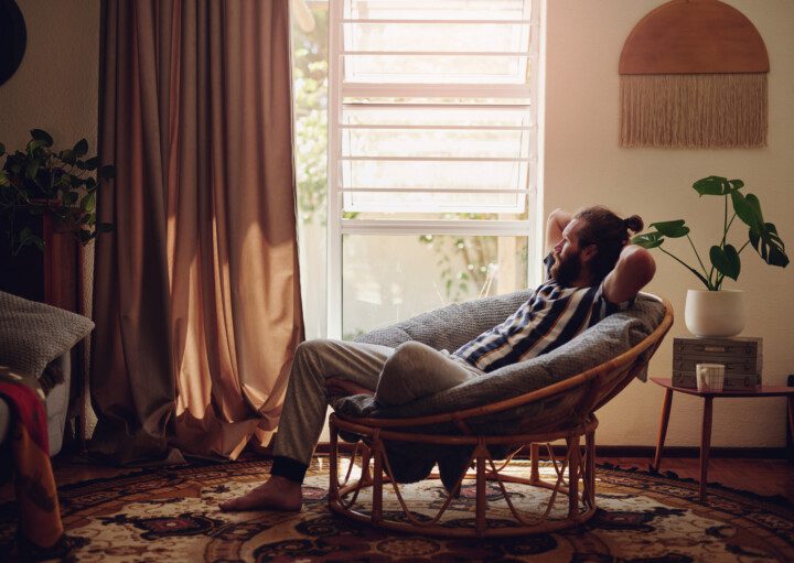 Imagem de uma homem sentado em uma poltrona de uma sala de estar com decoração em tons terrosos.