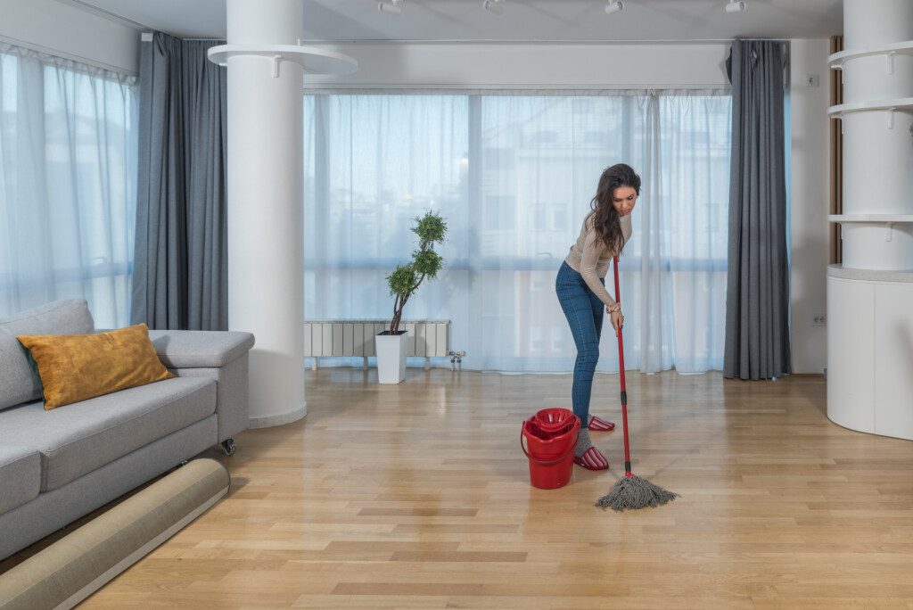 Foto que ilustra matéria sobre como limpar porcelanato mostra uma mulher passando um esfregão em um piso de porcelanato amadeirado.