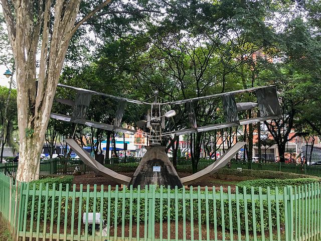 Uma grande escultura de relógio de sol com partes metálicas fica em um jardim circular cercado por árvores e vegetação — um local atraente se você estiver procurando o que fazer em São José dos Campos em um parque urbano.
