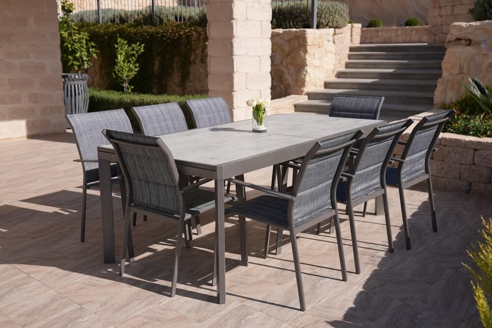 Foto que ilustra matéria sobre tipos de piso mostra um pequeno pátio externo ao lado de uma casa com piso de cerâmica e uma mesa com oito lugares com tampo também de cerâmica.