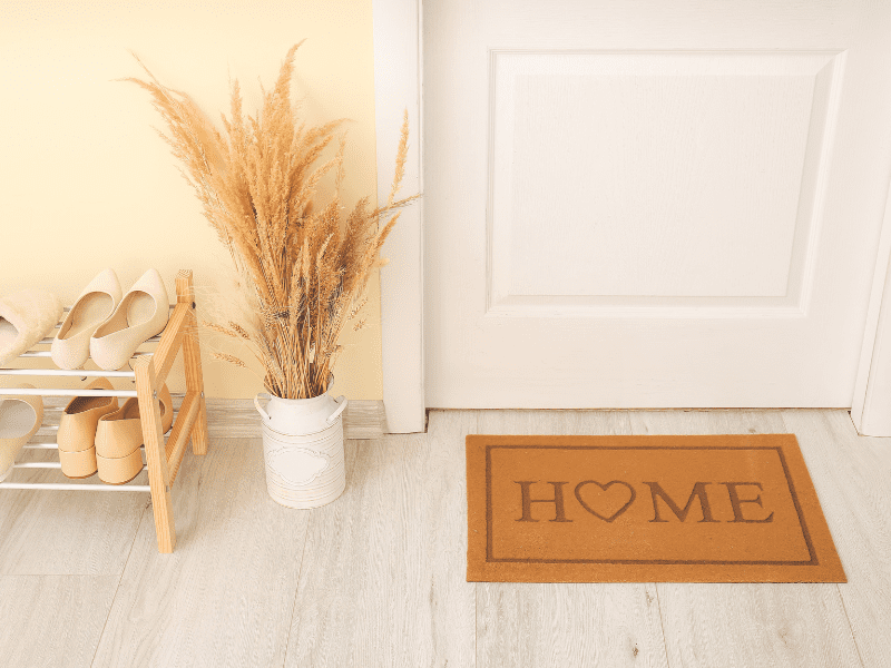 Hall de entrada decorado com trigo, tapete e porta calçados.