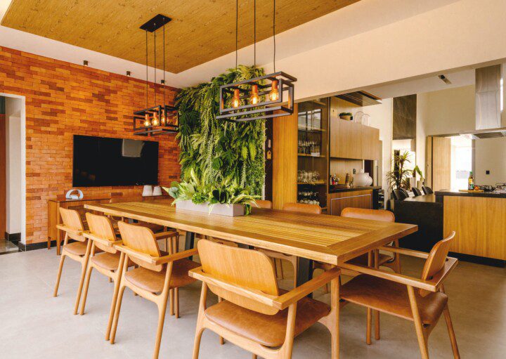 Decoração de área gourmet com mesão de madeira, teevisão ao fundo e lustre pendente com folhas. Foto disponível no Unsplash