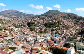 Imagem da vista aérea da cidade de Nova Lima mostra casas, avenidas e montanhas ao fundo em um dia de céu azul para ilustrar matéria sobre o que fazer em Nova Lima, Minas Gerais