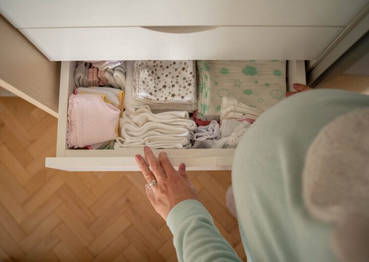 Imagem de uma mulher grávida abrindo uma gaveta da cômoda do bebê.