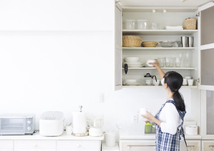 Imagem de uma mulher organizando um armário de cozinha.