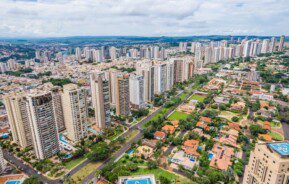 Foto que ilustra matéria sobre morar em Ribeirão Preto mostra uma visão do alto da Avenida Professor João Fiúza, a mais importante da cidade, com muitos prédios altos à esquerda e casas em zonas arborizadas à direita.