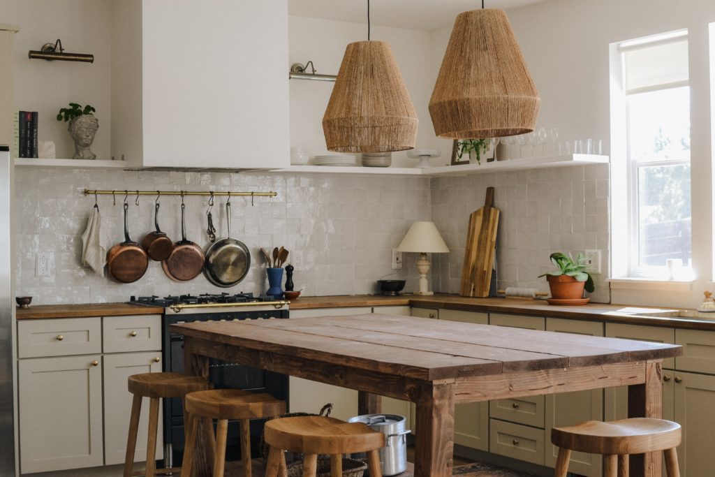 cozinha no estilo grego, com traços rústicos. Mesa e bancos de madeira e lustre de palha