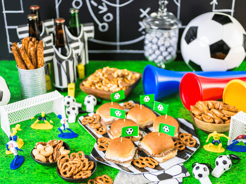 Mesa decorada com elementos do jogo de futebol: traves, jogares em miniatura, cores da bandeira do brasil e bola.