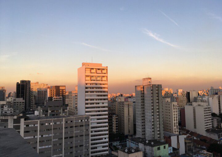 A imagem mostra a vista com prédios e casas no fim de tarde com o pôr do sol.