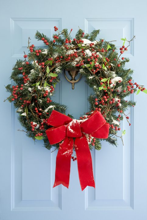 Guirlanda de Natal com um laço vermelho fixada em uma porta azul.