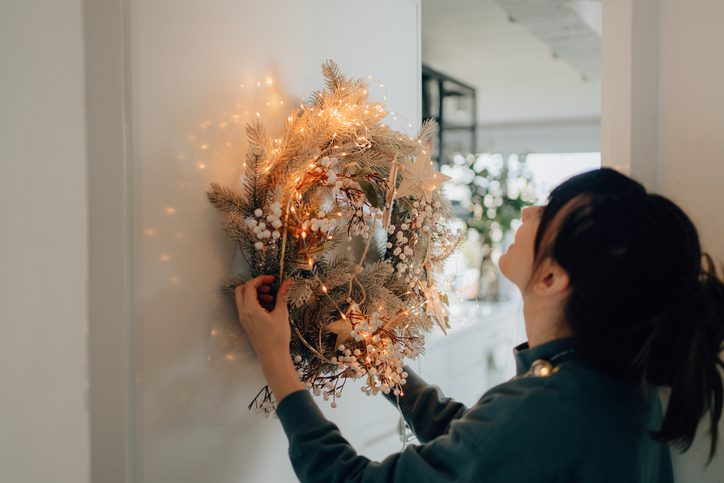 Mulher colocando uma guirlanda de natal com luzes pisca-pisca na porta de casa.