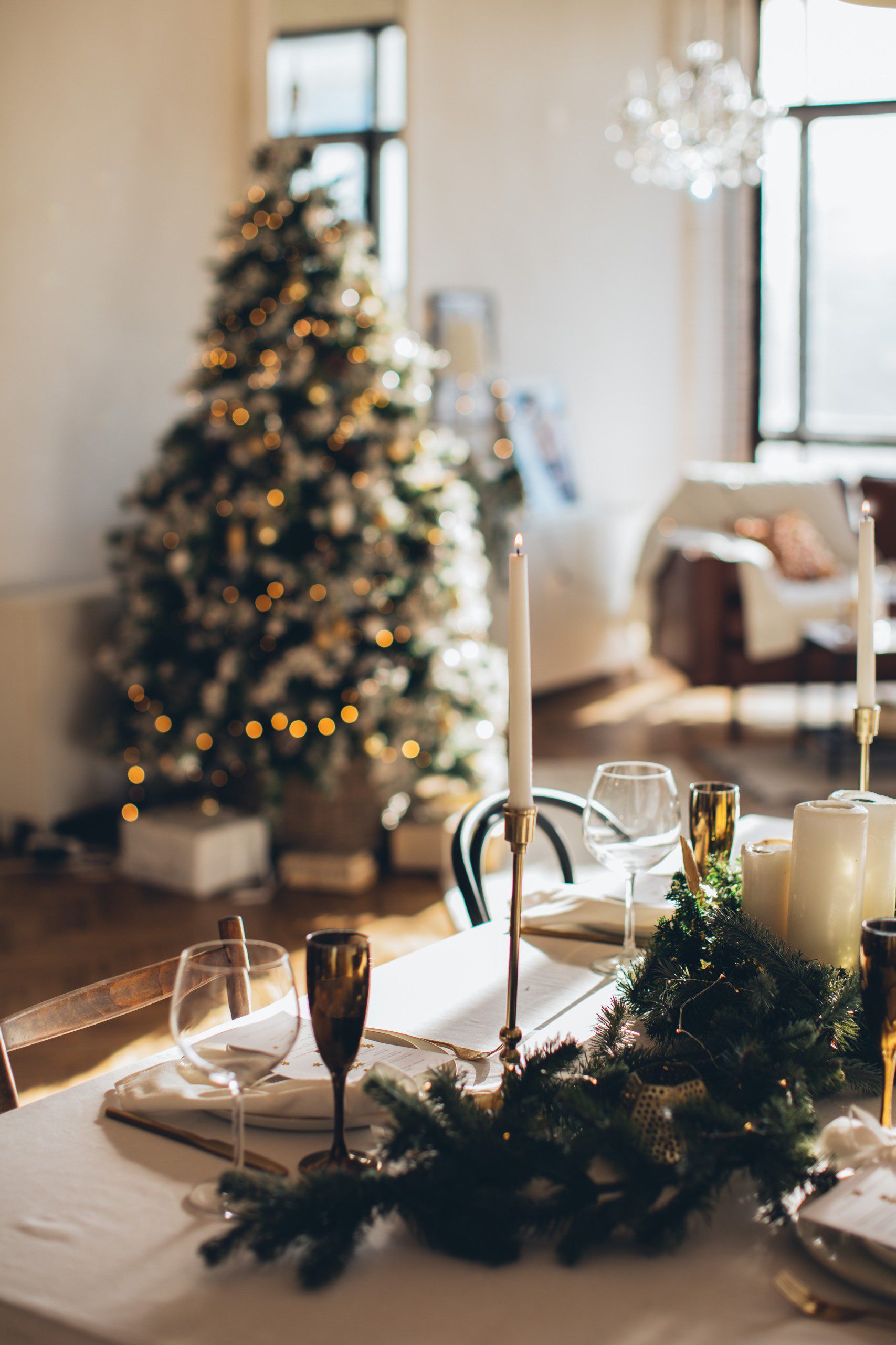 Mesa de Natal posta com uma árvore natalina com luzinhas e enfeites ao fundo.