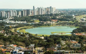 Imagem da vista aérea de Curitiba mostra lago, parque, vegetação, casas e prédios ao fundo para ilustrar matéria sobre qual o bairro mais seguro de Curitiba