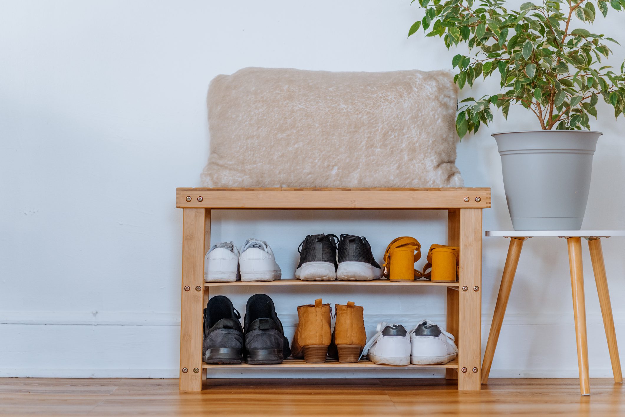 Imagem de uma sapateira feita em padeira com sapatos e uma planta em cima de uma mesa lateral. 