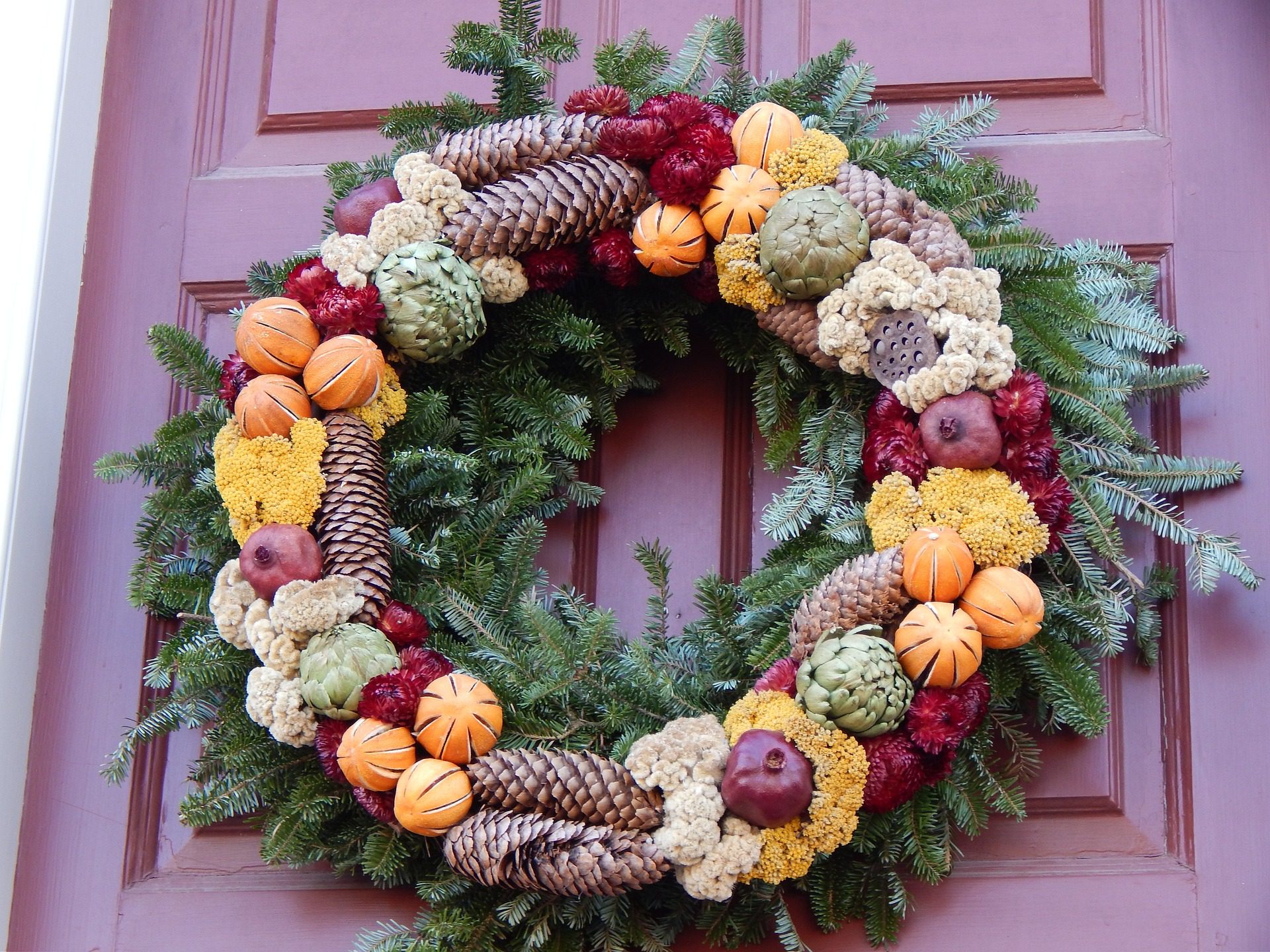 Guilanda de Natal com pinhas e flores em uma porta bordô.