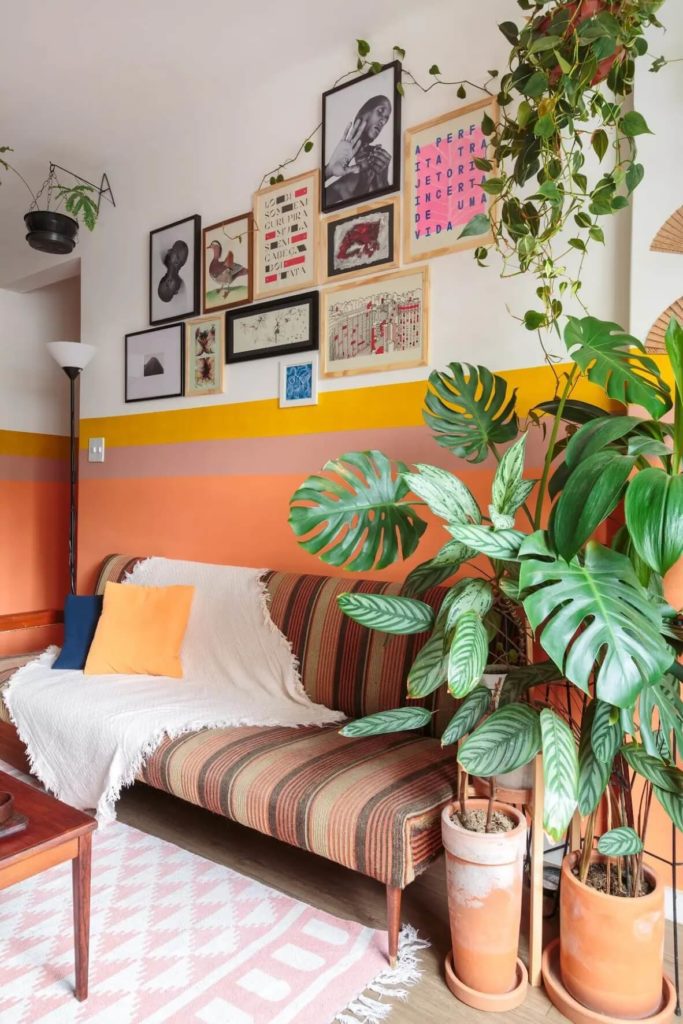 Foto que ilustra matéria sobre pintura setorizada mostra uma sala de estar com uma parede pintada de branco do meio para cima, com duas listras amarela e bege no meio e toda de laranja claro do meio para baixo.