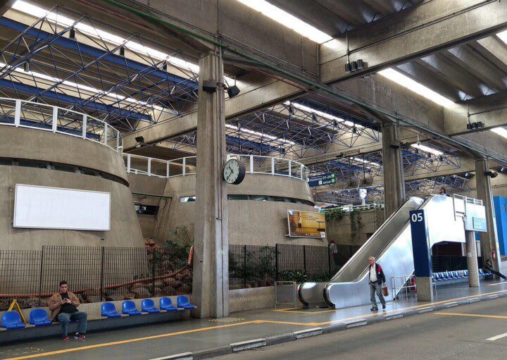 Foto mostra uma estrutura coberta do Terminal Jabaquara, com um nível mais baixo na altura da rua e uma escada rolante que leva ao nível de cima.