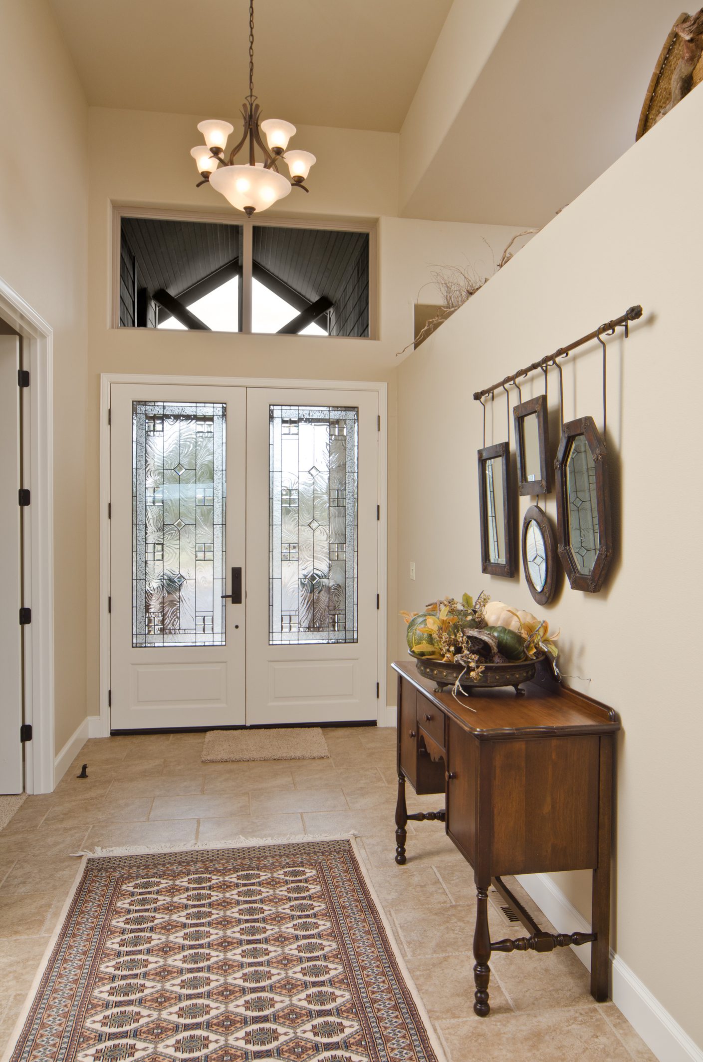 Foto de um corredor onde foram colocados quatro quadros de diferentes tamanhos e formatos: quadrado, redondo e hexágono. Eles estão pendurados na parede, formando uma bela composição. Há também na imagem um aparador, com um enfeite em cima, além de um tapete.